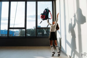 Girl tossing backpack in sunlight.